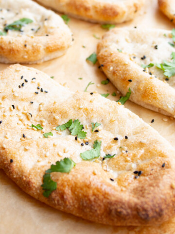 A naan bread topped with black and white sesame seeds and chopped coriander.