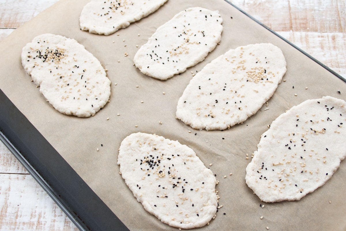 Unbaked naan breads on a baking sheet.