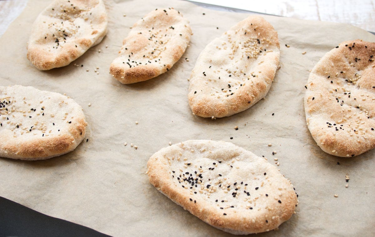 Baked naan breads on a baking sheet.