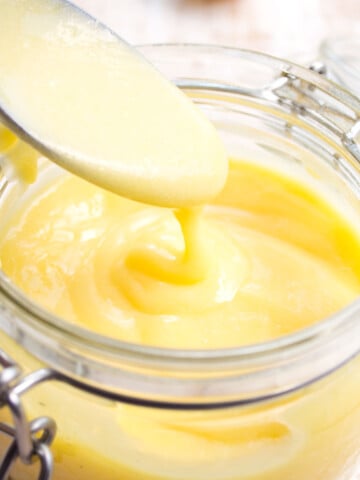 S glass jar with lemon curd and a spoon.