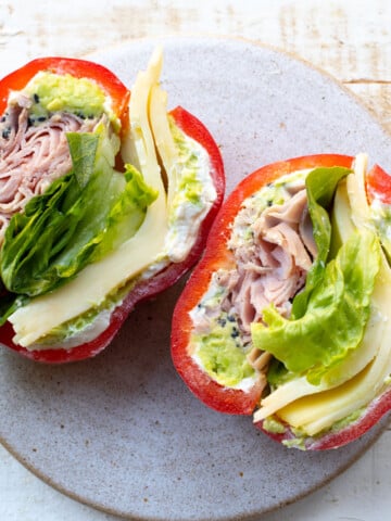 A bell pepper sandwich filled with ham, sliced cheese, lettuce, avocado and cream cheese.