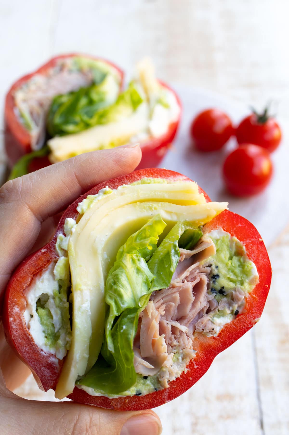 Hand holding a pepper sandwich filled with ham, cheese and more.