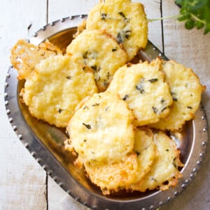 Coconut crackers topped with melted cheese and fresh thyme in a silver serving bowl.