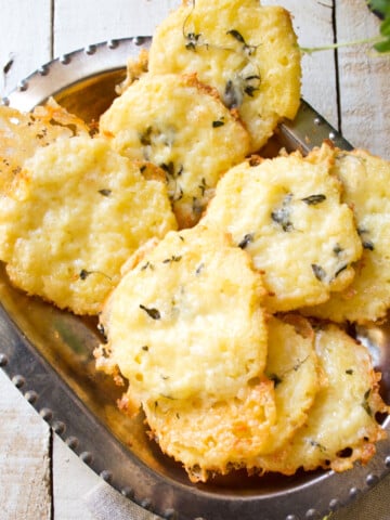 Coconut crackers topped with melted cheese and fresh thyme in a silver serving bowl.