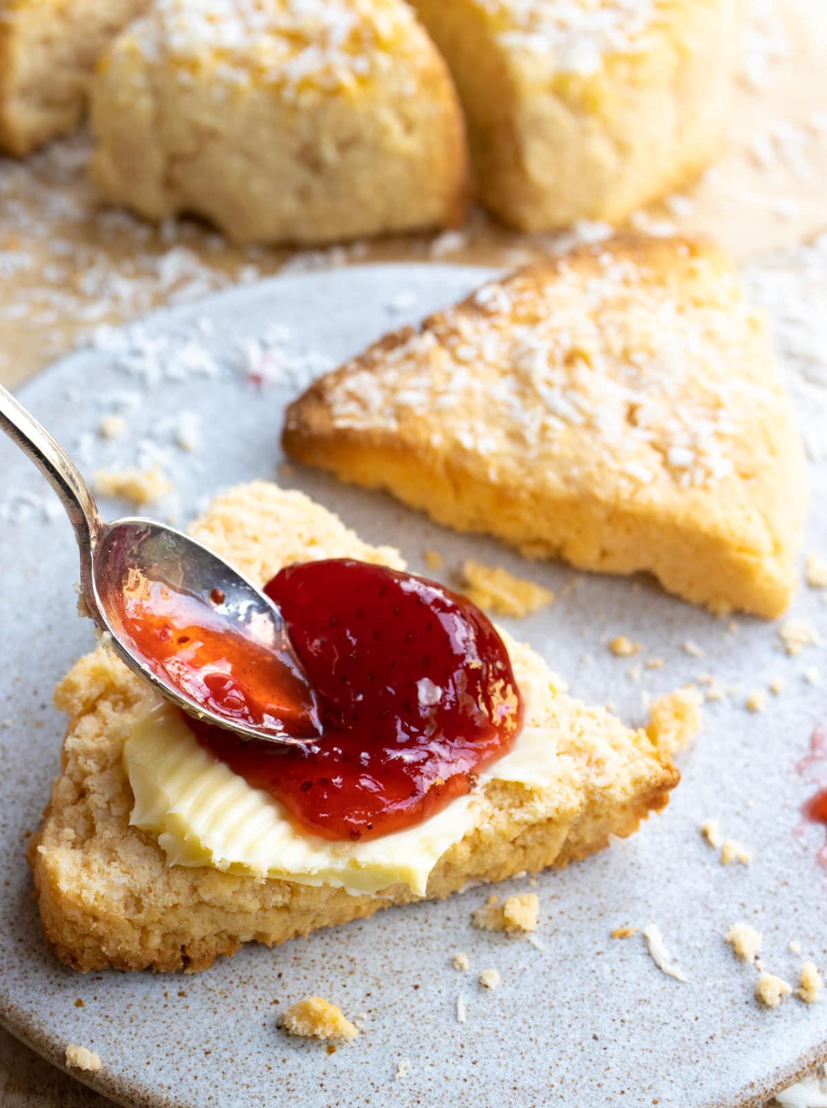 A scone sliced in half and topped with butter and strawberry jam.