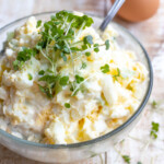 A bowl with egg salad and a spoon.