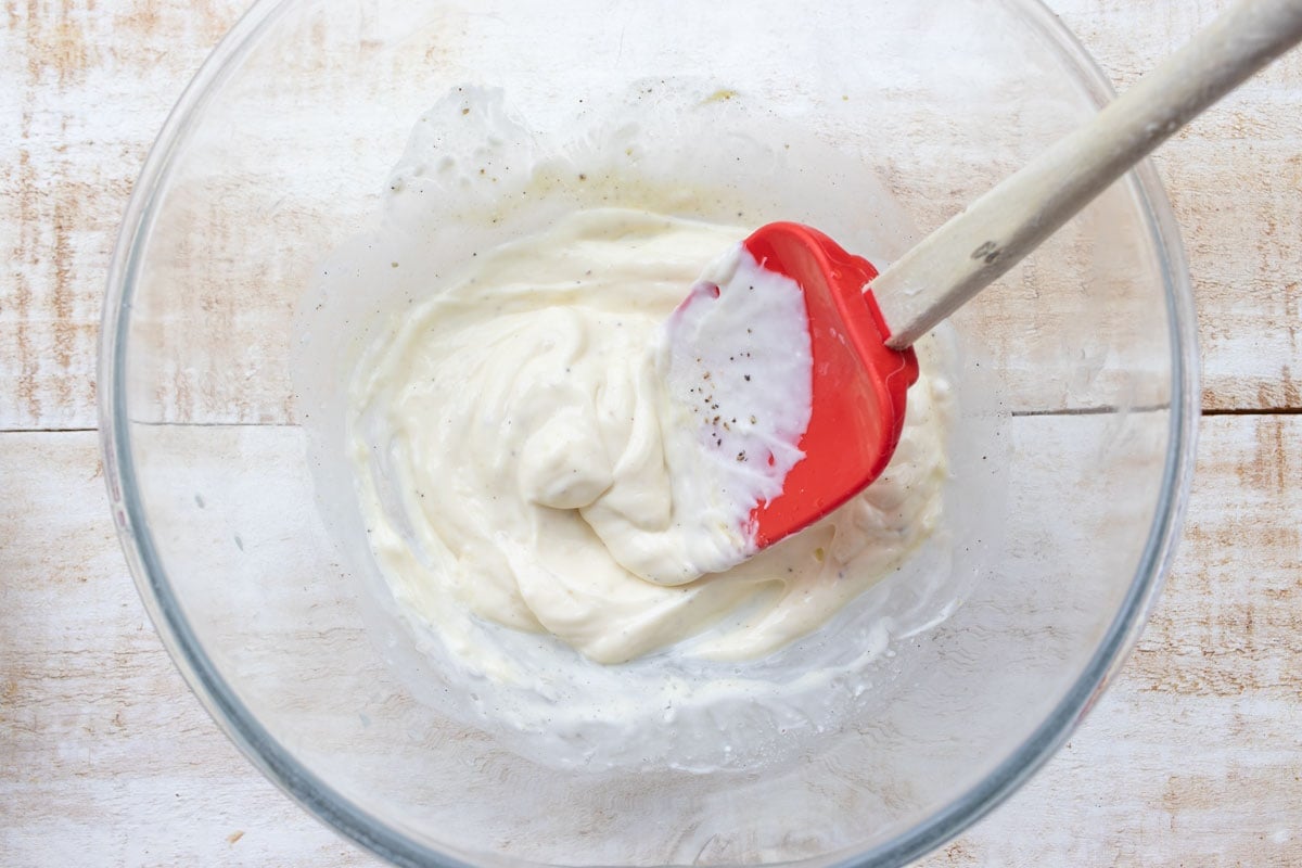 Stirring lemon juice and mustard into mayonnaise in a bowl with a spatula. 