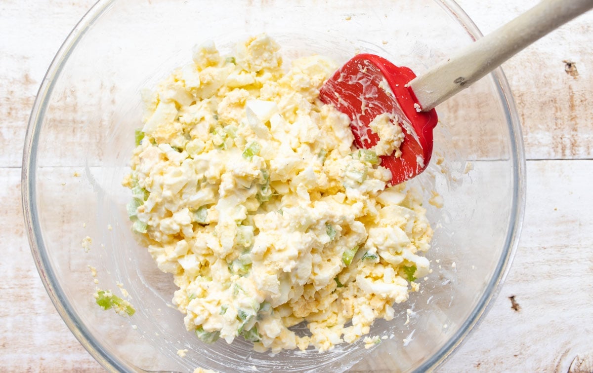 Stirring the egg salad in a bowl with a spatula. 