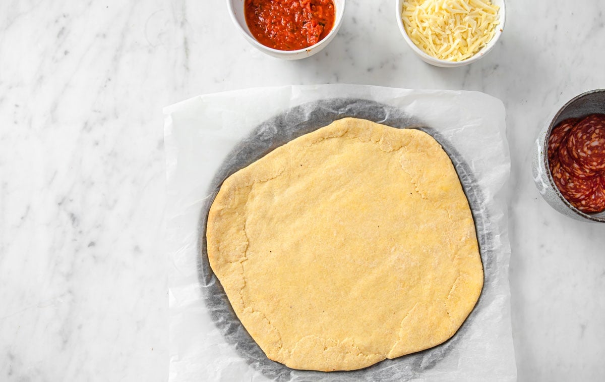Pre-baked pizza base with topping ingredients in bowls.