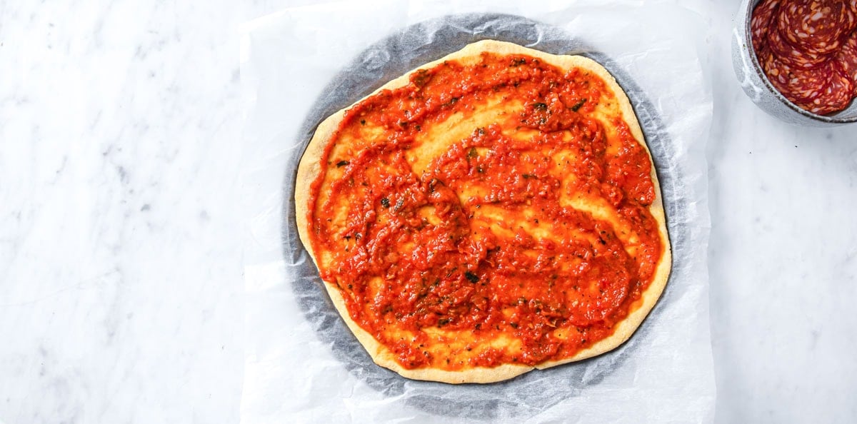 Pre-baked pizza crust spread with pizza sauce.