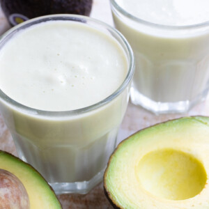 Frothy avocado milk in a glass and halved avocados.