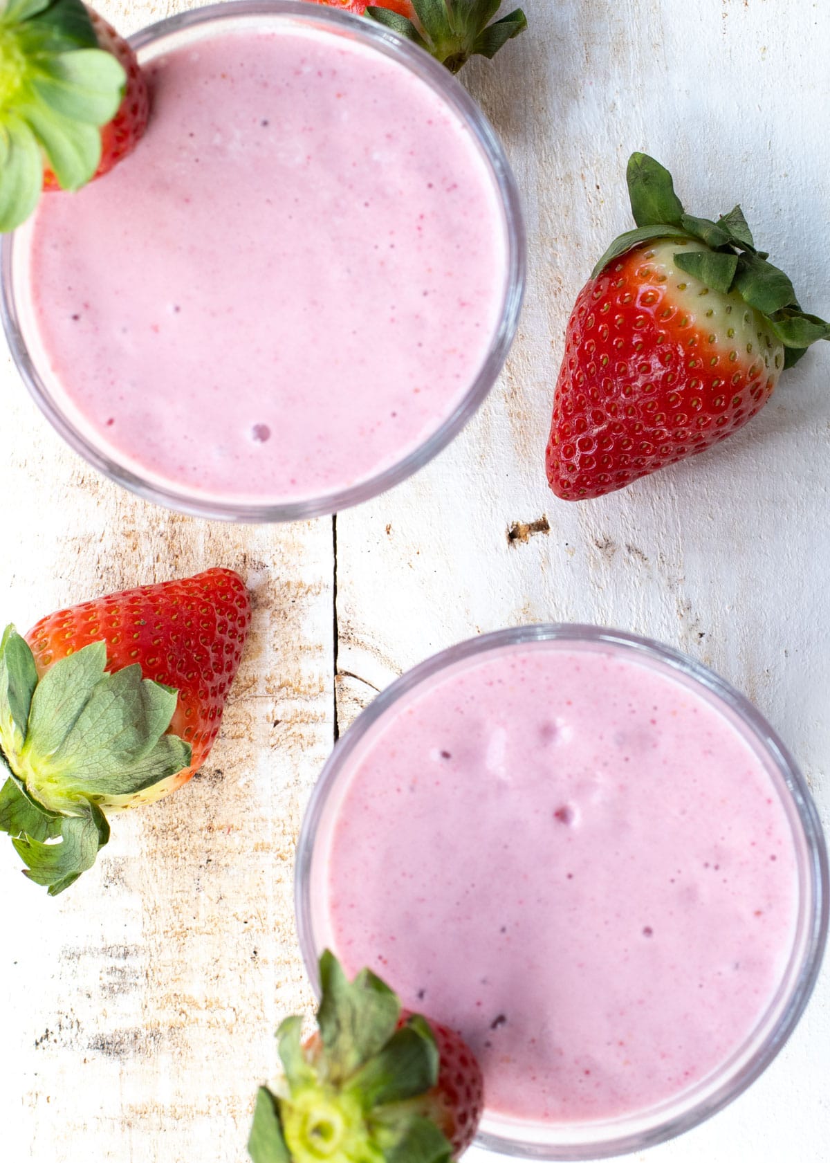 Two glasses with strawberry smoothie and fresh strawberries.