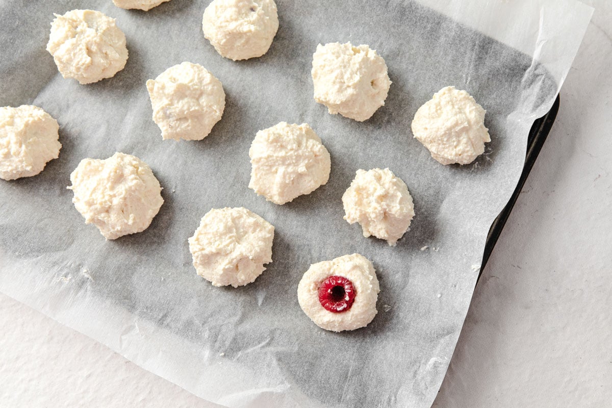 Cheesecake balls on a tray with parchment paper, with a raspberry pressed into the centre.