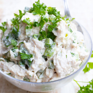 A bowl filled with mayonnaise chicken salad topped with chopped parsley.