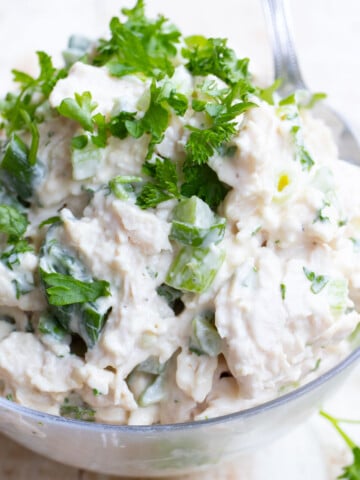 A bowl filled with mayonnaise chicken salad topped with chopped parsley.