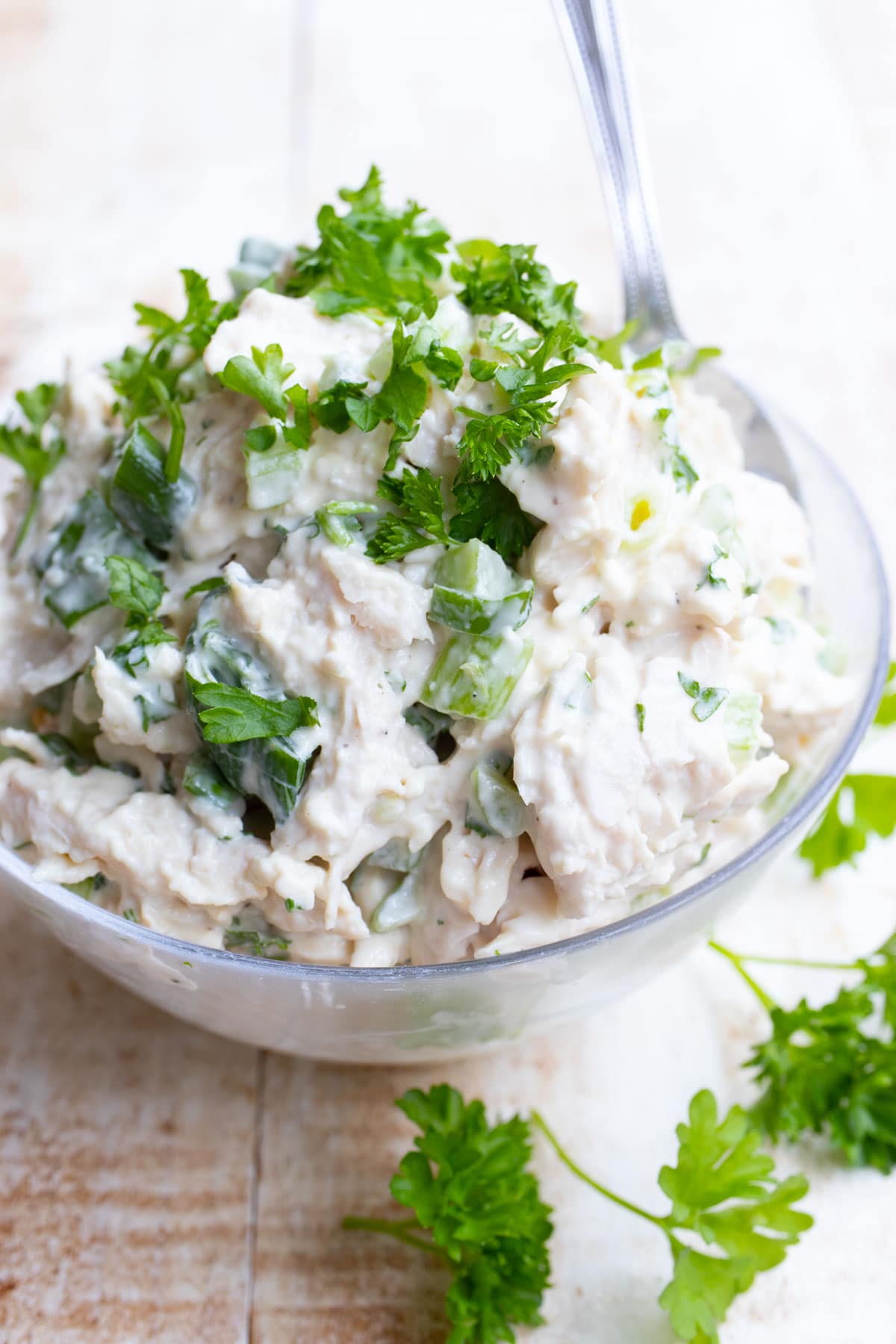 A glass bowl with chicken salad topped with parsley.