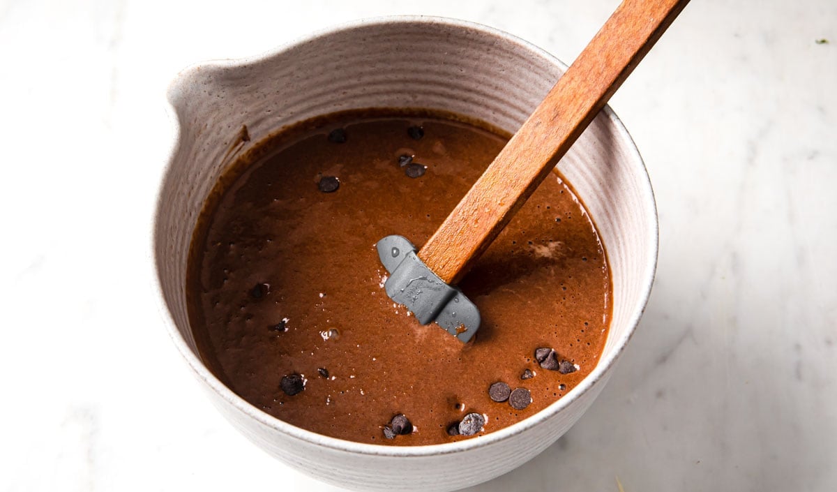 A bowl with chocolate batter with chocolate chips and a spatula.