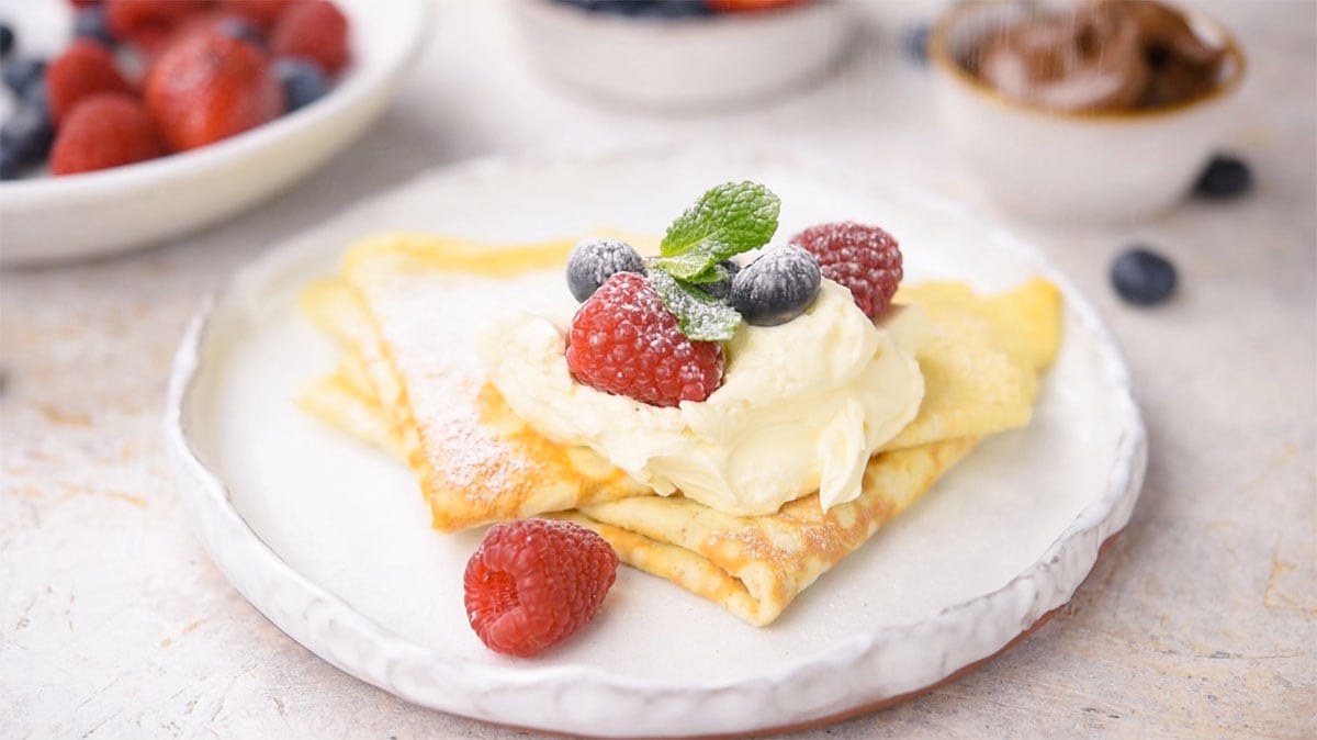 Folded crepes topped with cream and berries on a plate.