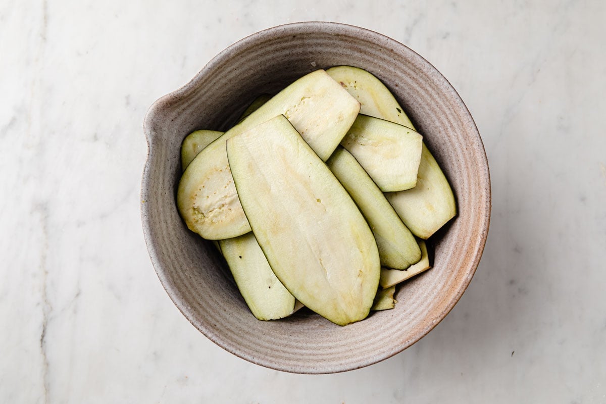 sliced raw eggplant with salt in a bowl.