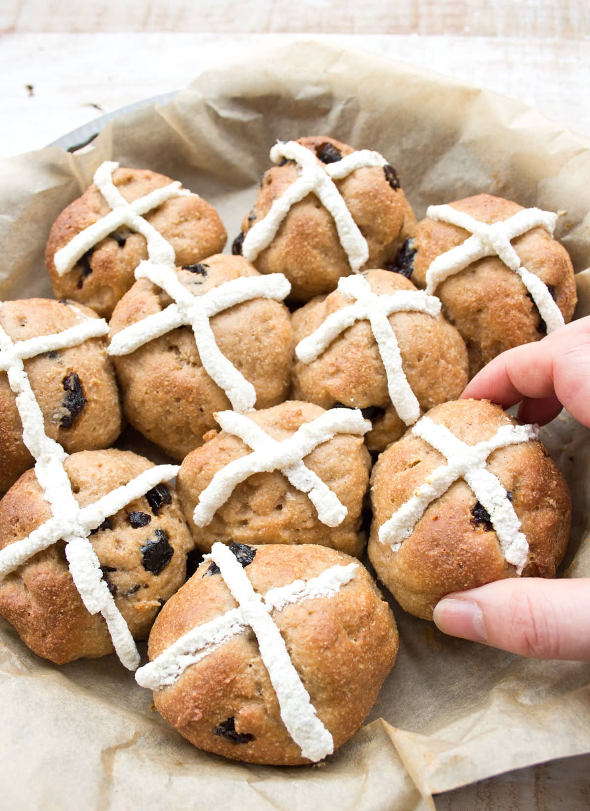 Picking up a hot cross bun from a baking pan.