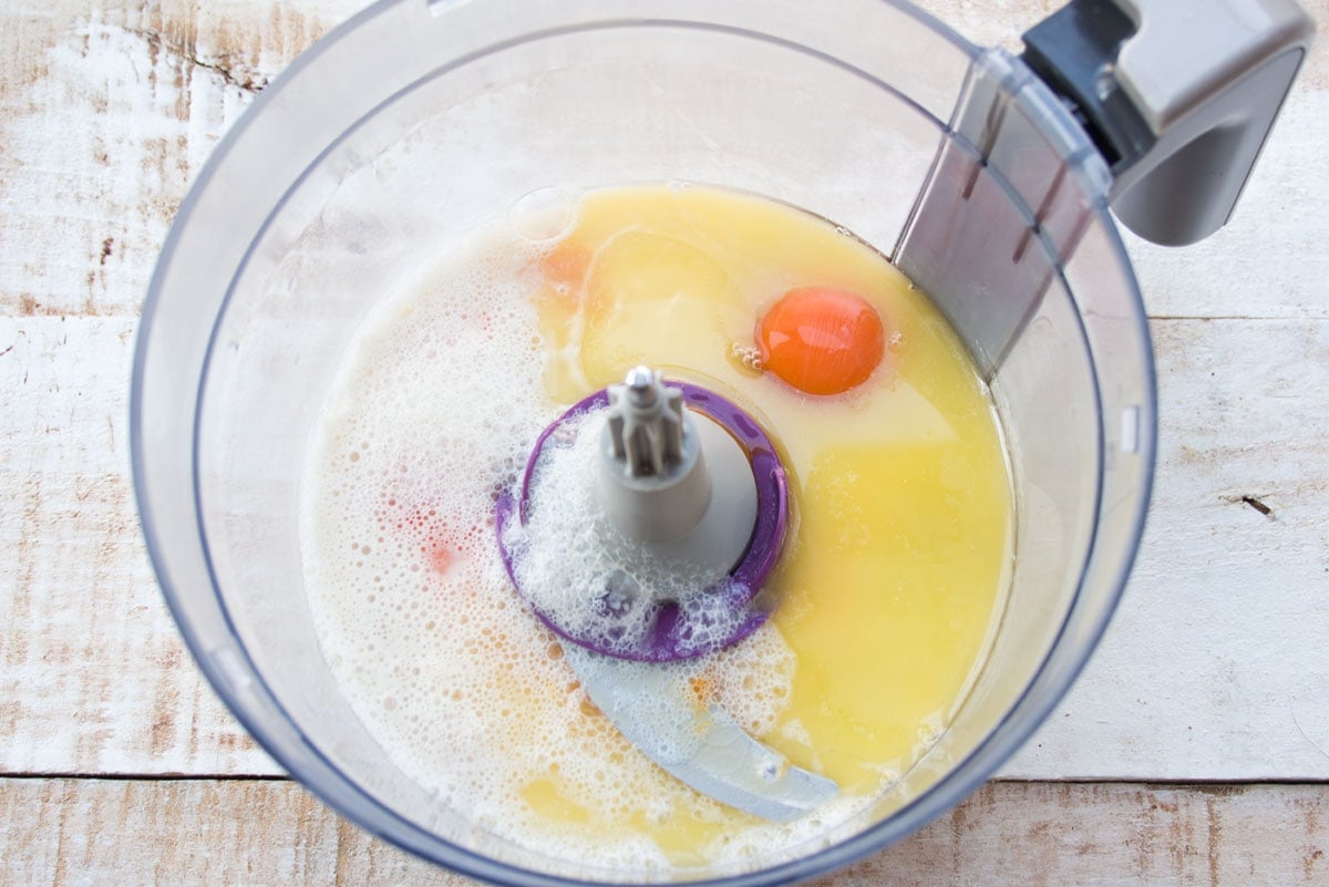 Blending eggs and other wet ingredients in a food processor bowl.