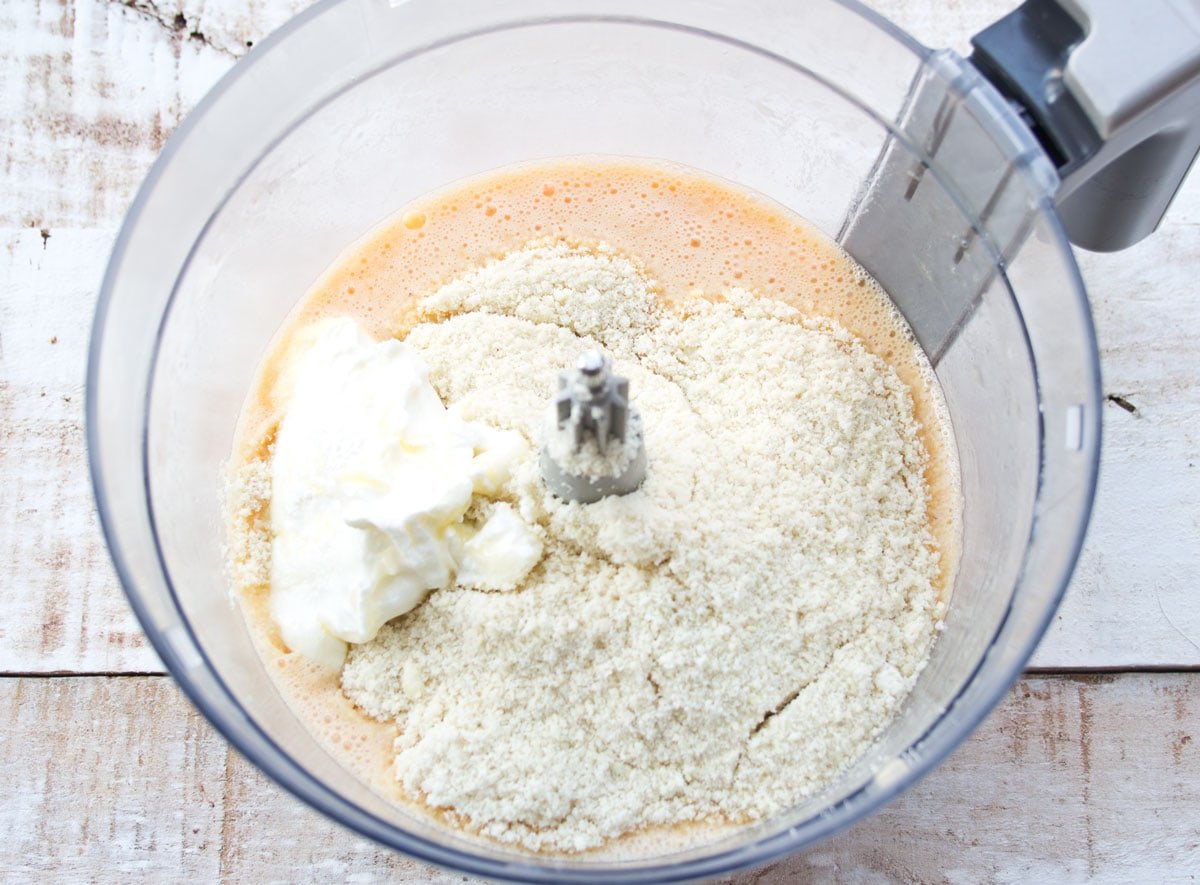 Adding almond flour to the egg mixture in a food processor bowl.