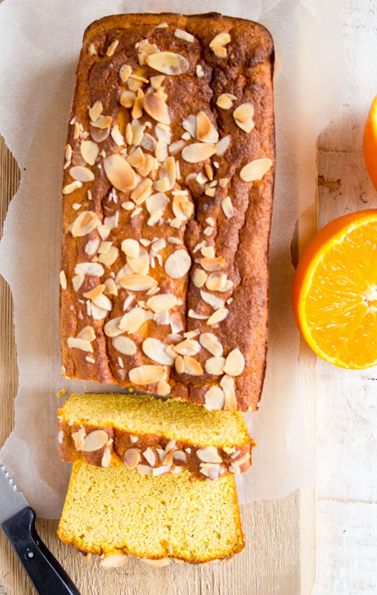 A rectangular loaf cake topped with almonds and halved oranges on the side.