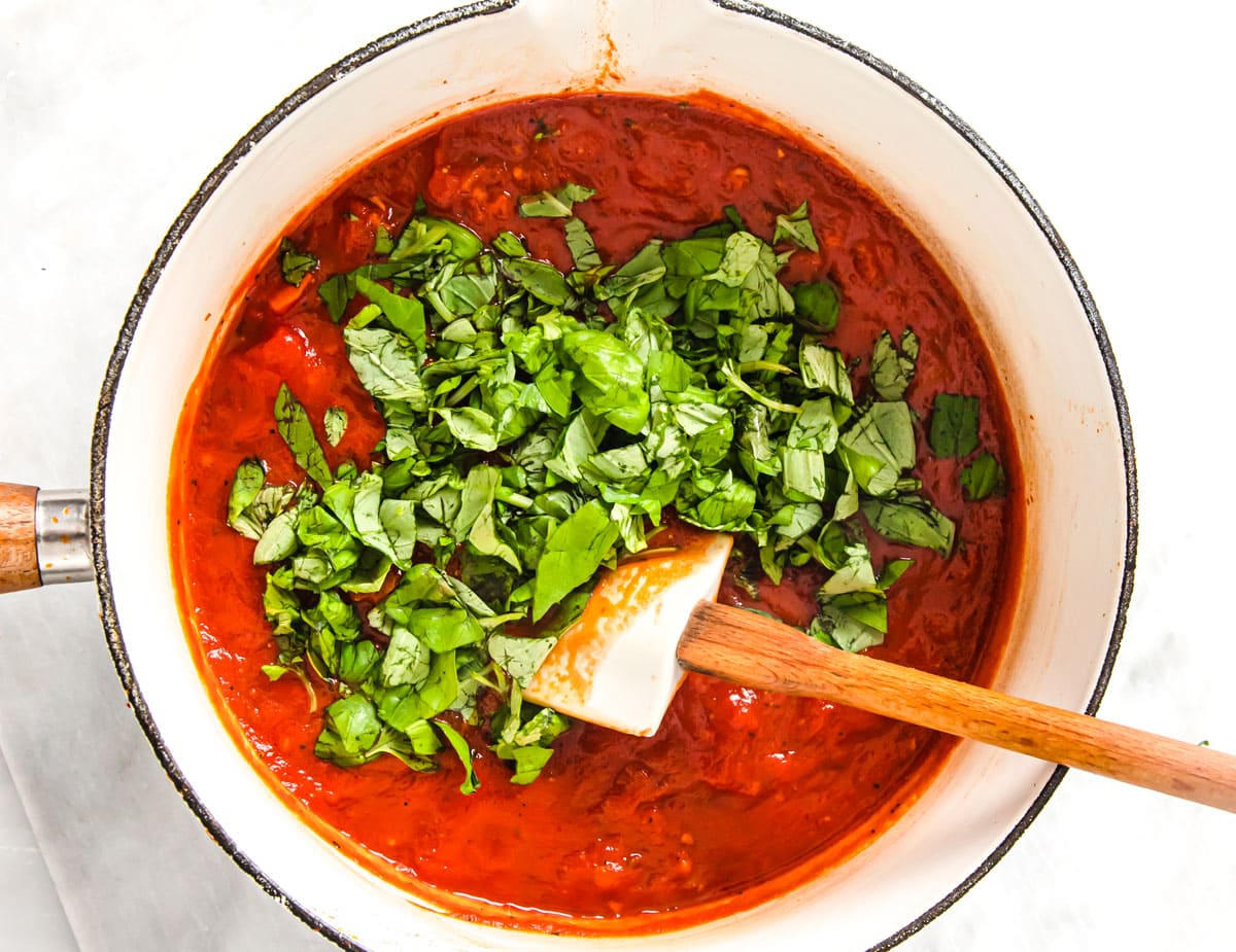 Adding chopped fresh basil to the tomato sauce in a saucepan.