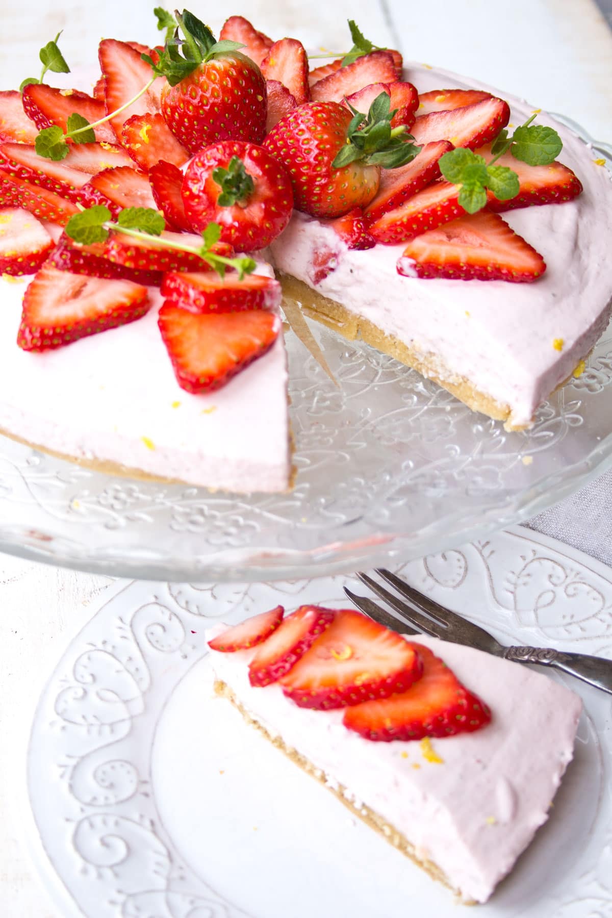 A strawberry cheesecake on a cake stand and a slice of cheesecake on a plate.