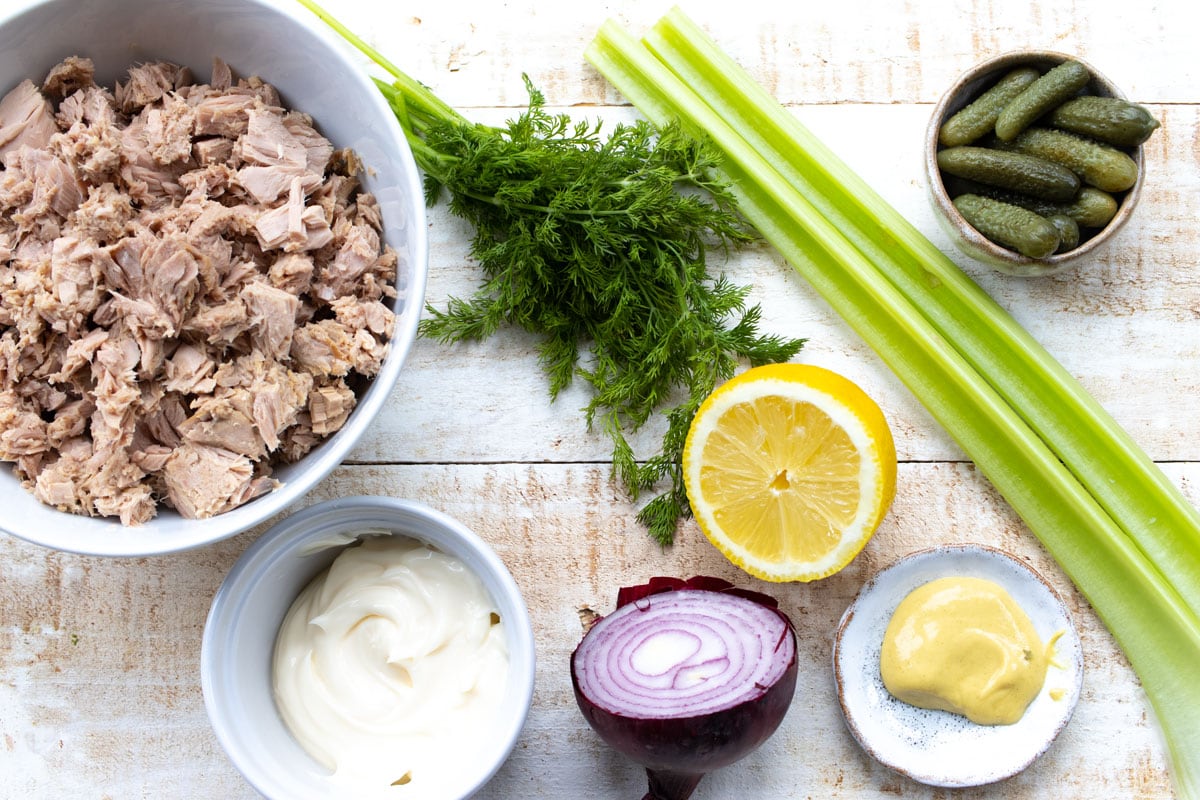 Ingredients for this recipe measured into bowls, such as tinned tuna, mayonnaise, celery stalks and onion.