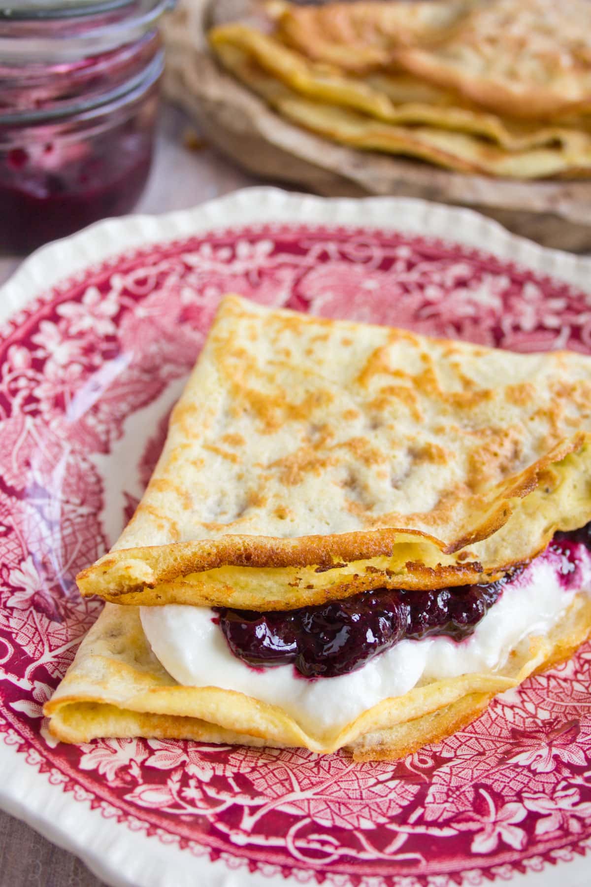 Folded crepe on a plate filled with yogurt and jam.