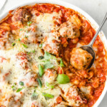 Meatballs in tomato sauce with melted cheese in a round dish and a spoon with a meatball.