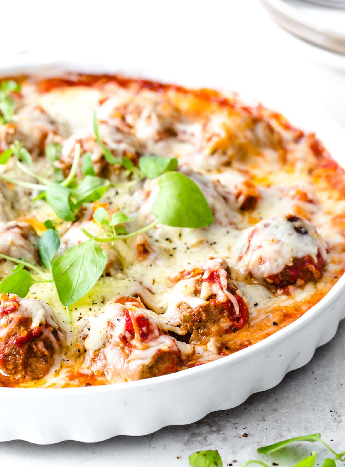 Meatballs in a round casserole in tomato sauce topped with cheese.