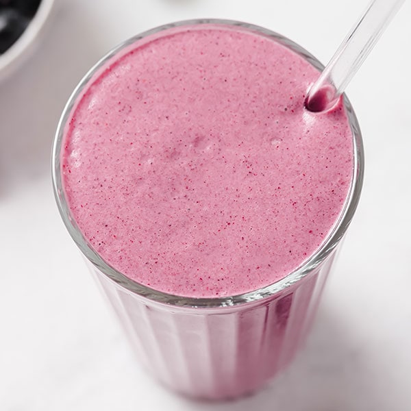 A berry smoothie in a glass with a straw.