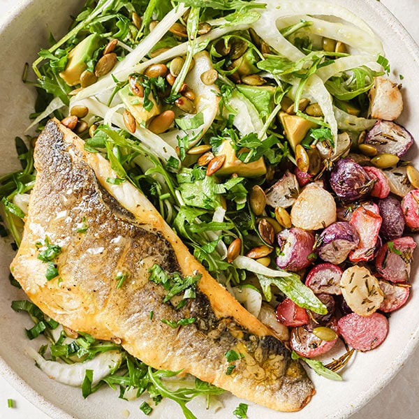 A sea bass fillet on a bed of rucola and fennel salad with roasted radishes.