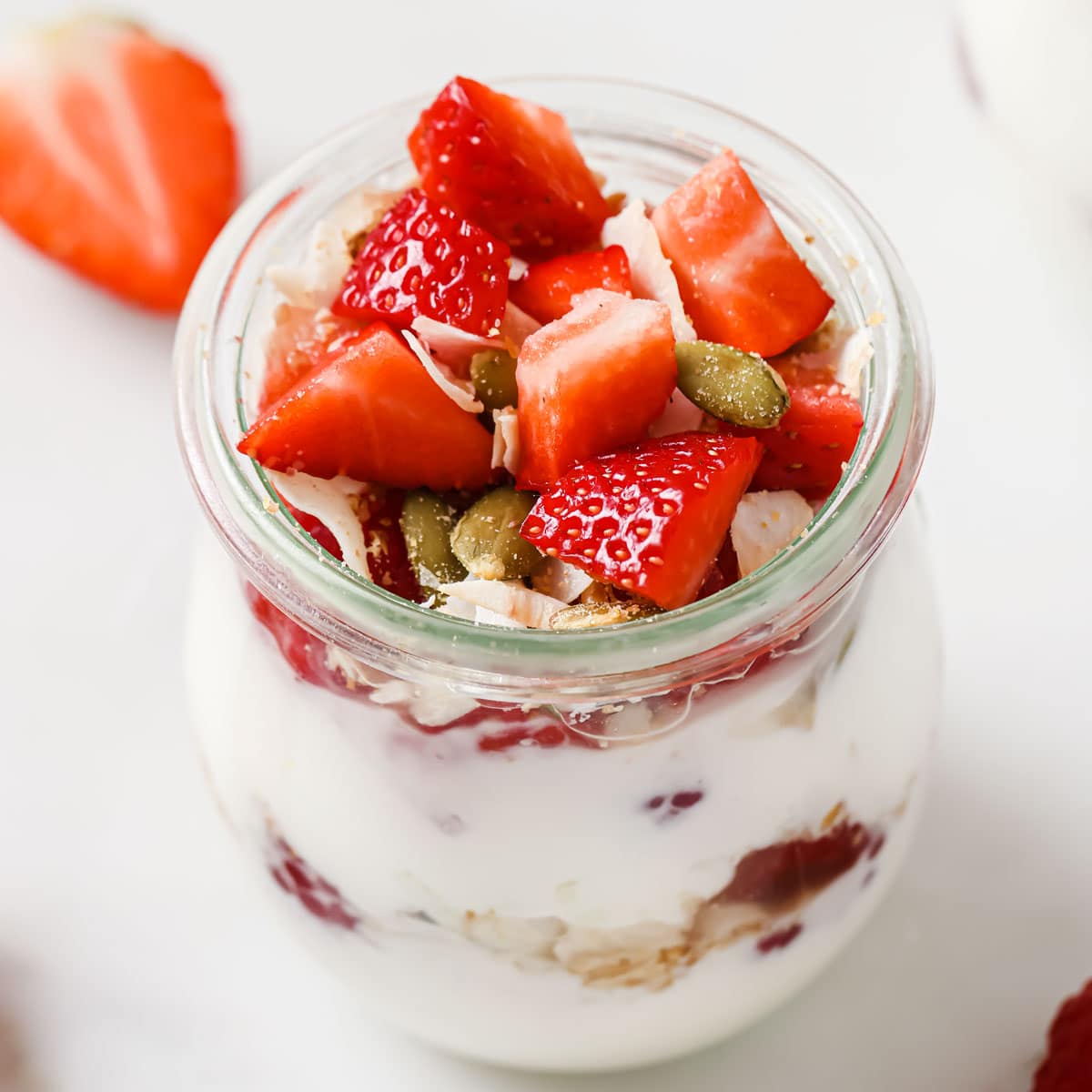 A glass jar with coconut yoghurt parfait and strawberry topping.