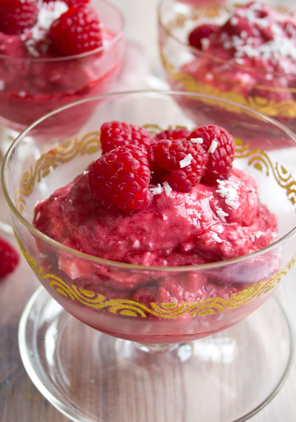 A glass bowl with frozen raspberry yogurt topped with raspberries.