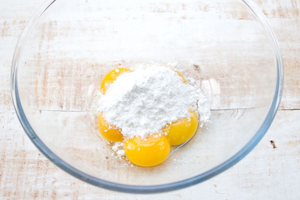 Egg yolks and powdered sweetener in a glass mixing bowl.