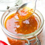 A mason jar with sugar free sweet chili sauce and a spoon.