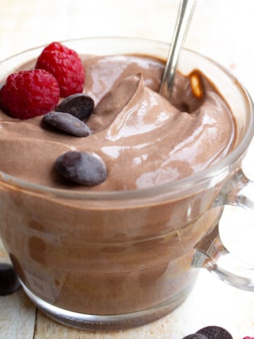 A glass cup with chocolate yogurt and a spoon.