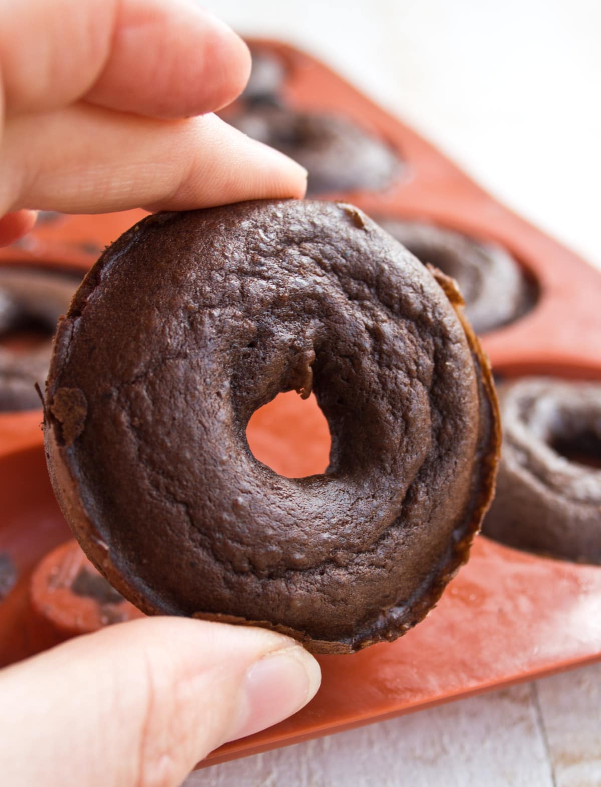 Hand holding a baked chocolate donut.