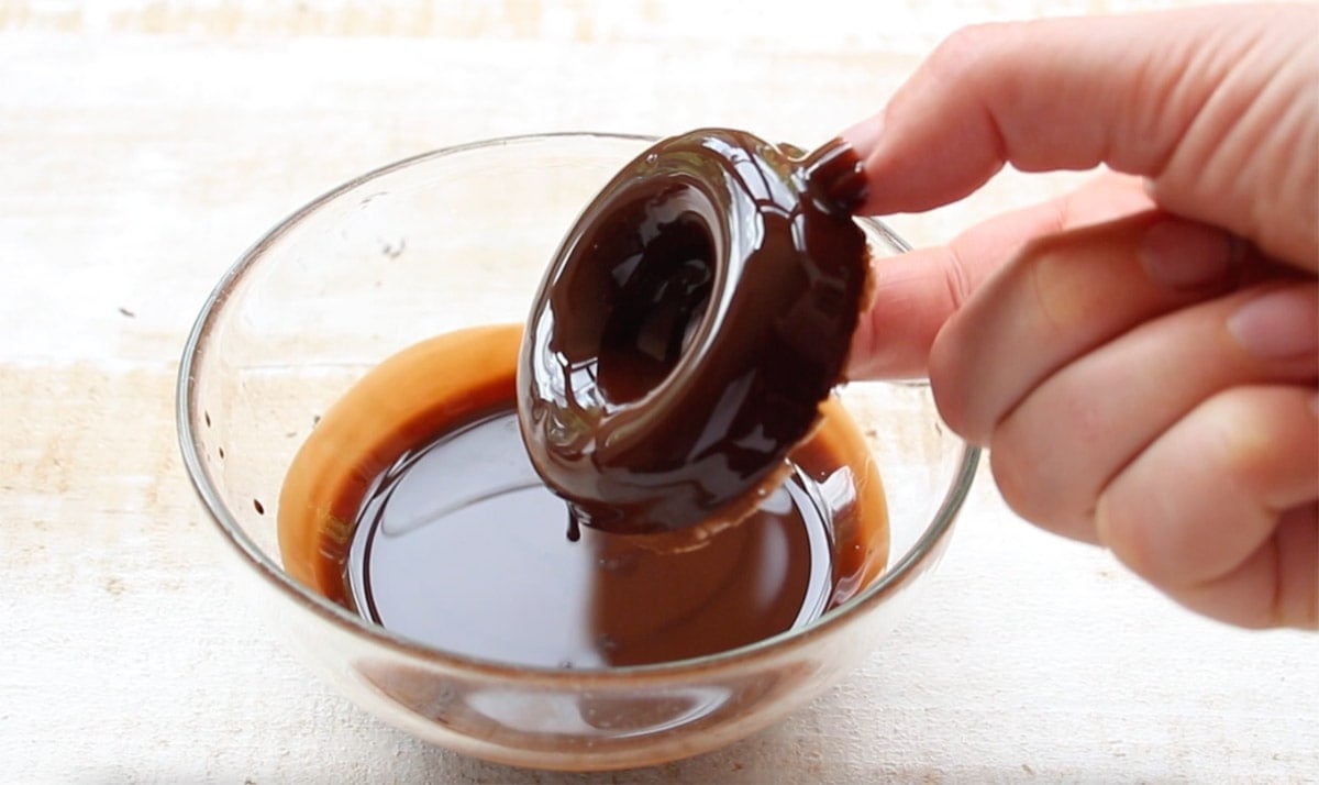 Dipping a donut into melted chocolate.