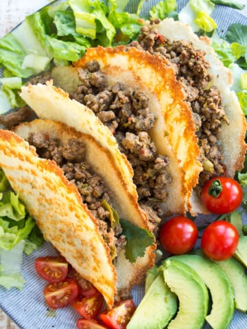 Three keto taco shells filled with beef and lettuce on a plate.