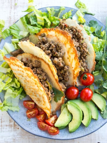 Taco shells filled with ground beef and lettuce on a plate.