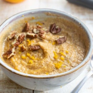 A bowl of pumpkin porridge topped with pecans.