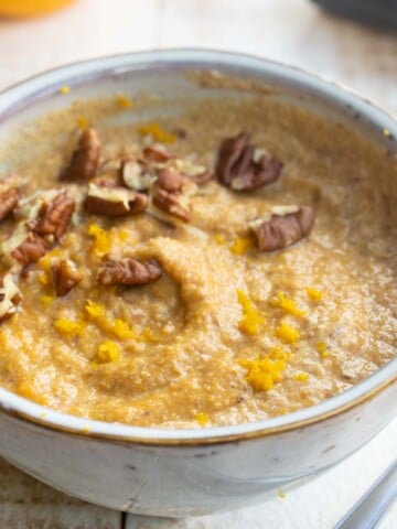 A bowl of pumpkin porridge topped with pecans.