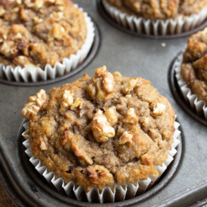 A coconut flour banana muffin in a muffin pan, topped with chopped walnuts.