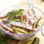 A bowl with a salad made from sliced sausage, pickles, onions and fresh dill.
