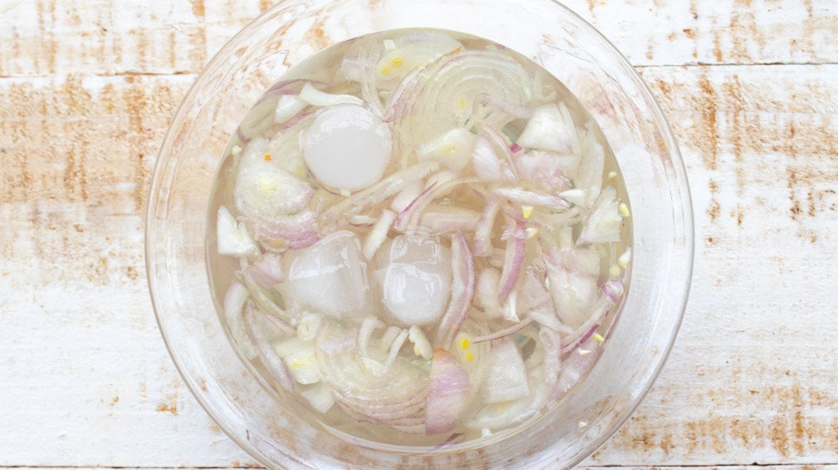 Sliced onions in a glass bowl filled with water and ice cubes.
