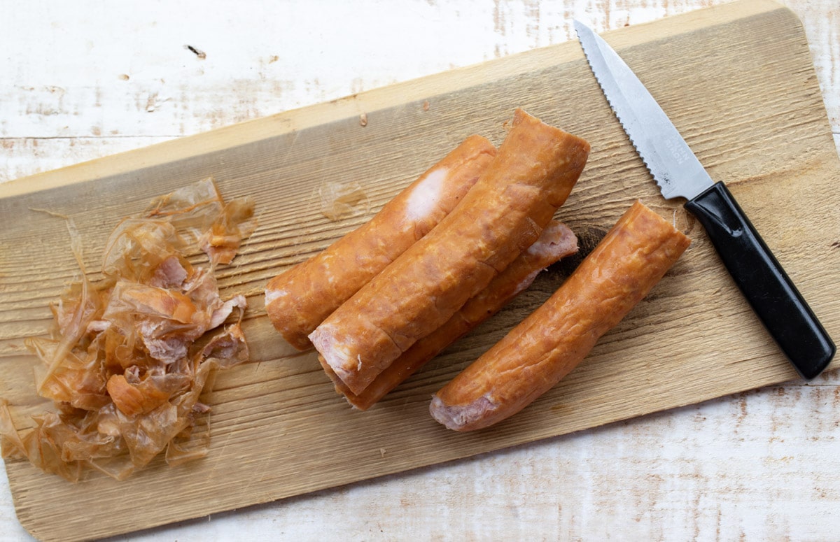Sausages on a wooden board with a knife and the removed casings.